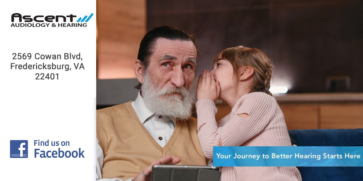 Slow motion of cute joyful 12-aged girl with funny pigtails which whispering on granddad's ear her secret while they sitting together on the sofa at home