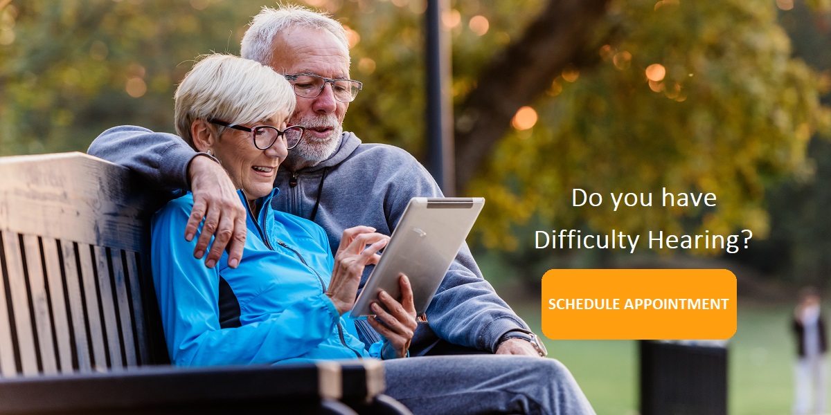 Smiling senior active couple sitting on the bench looking at tab